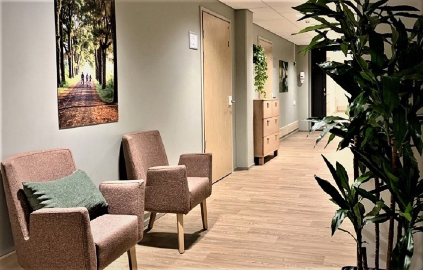 Onnikoti Jokipuiston sisätilat, käytävä, jossa kaksi tuolia ja viherkasvi.