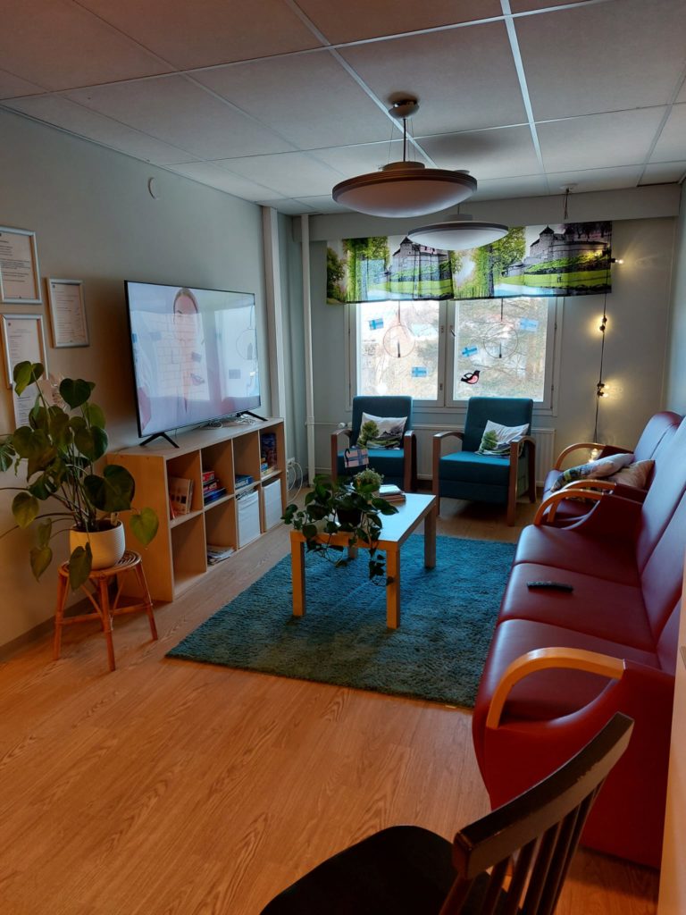 Onnikoti Kaurialan olohuone, iso ikkuna ja punainen sohva, taulutelevisio, kasveja