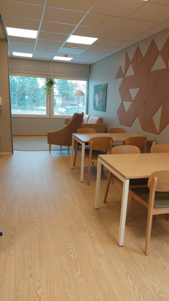 Onnikoti Apilan oleskelutila, jossa kaksi ruokailuryhmää, nojatuoli ja sohva.