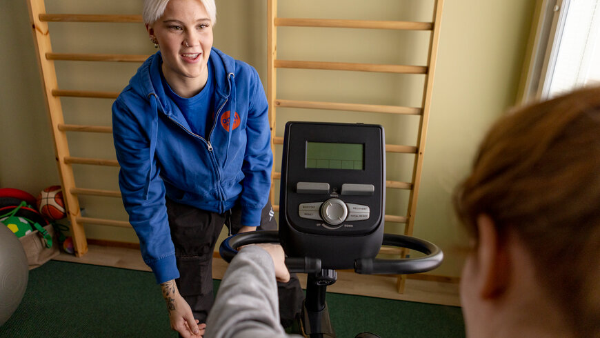 Lähihoitaja avustaa asukasta kuntosalilla