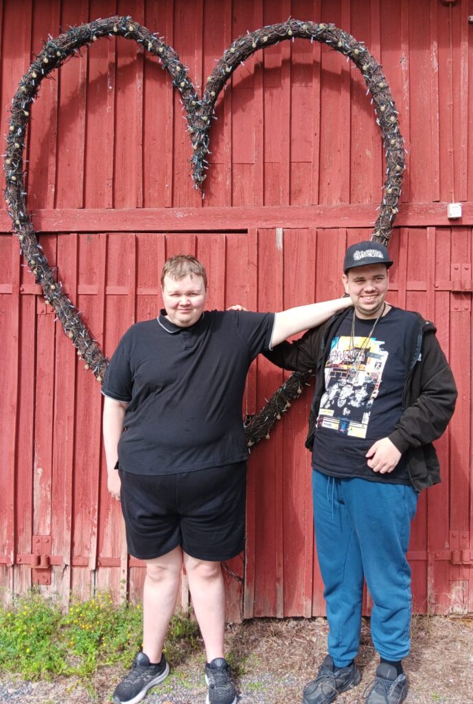 Onnikoti Jukolan asukkaat punaisen puuseinän edessä. Taustalla suuri sydän.