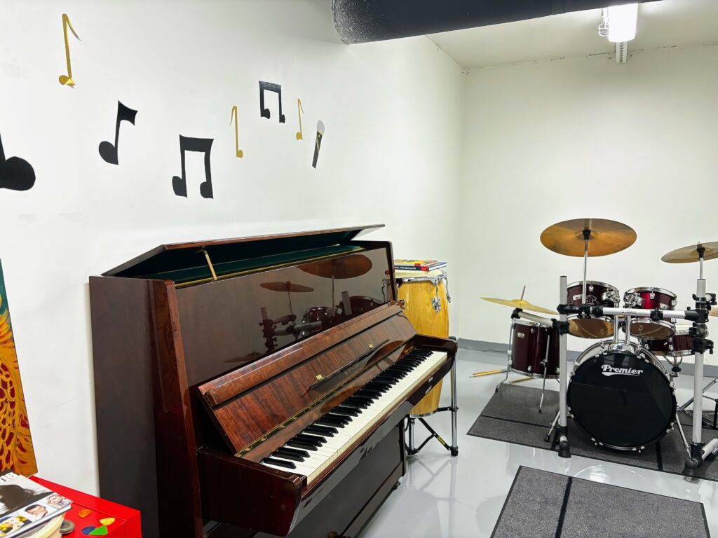 Musiikkihuone, ruskea piano, iso rumpu, nuotteja seinällä.