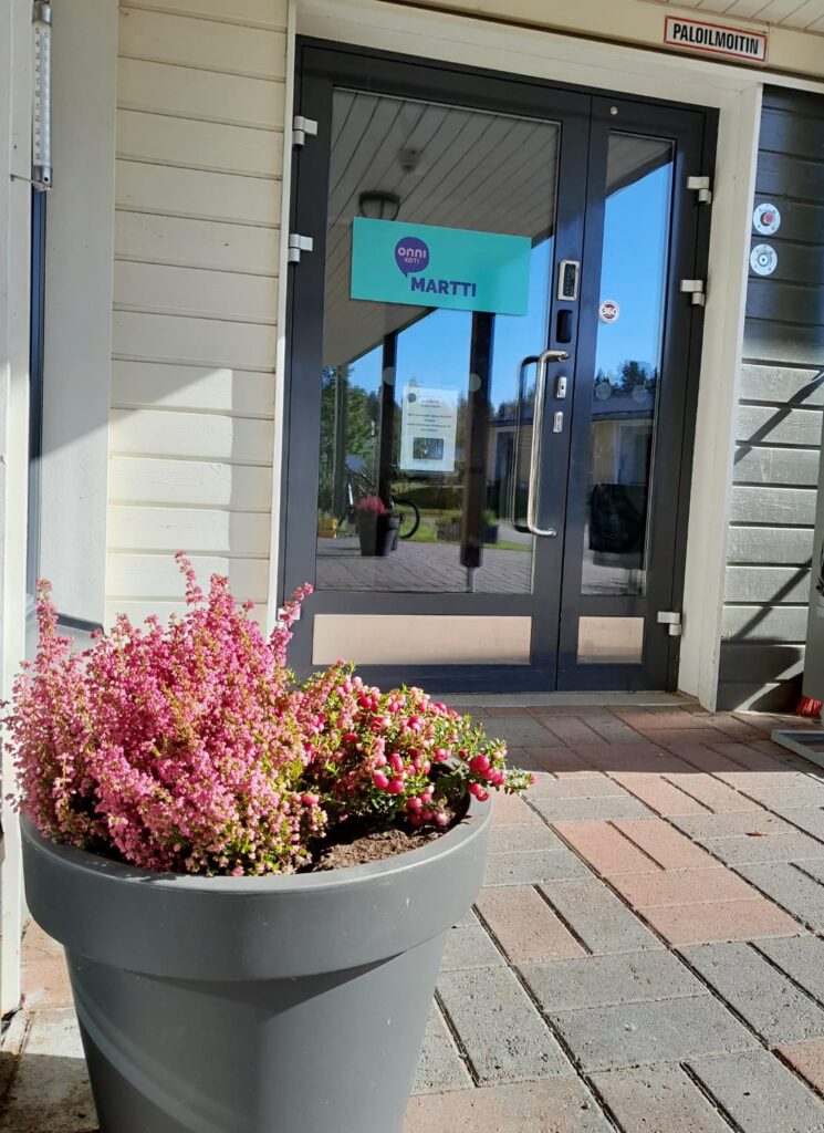 Onnikoti Martin sisäänkäynti, punertavia kasveja ruukussa ja pihakivetystä