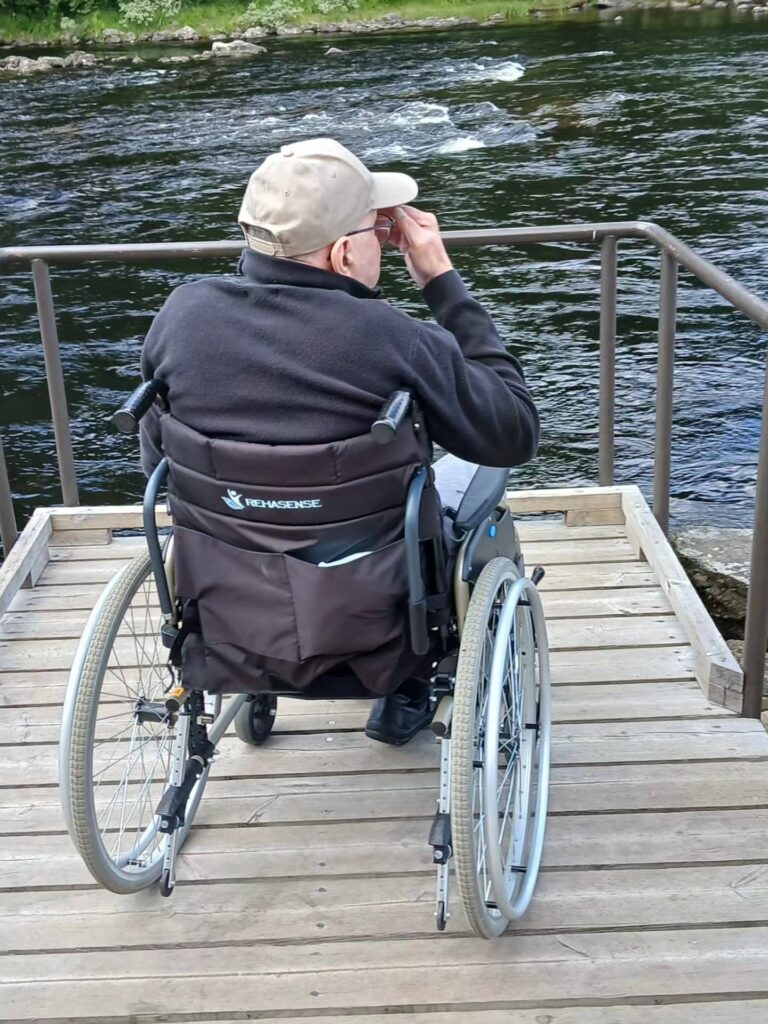 Henkilö istuu pyörätuolissa laiturilla veden äärellä.