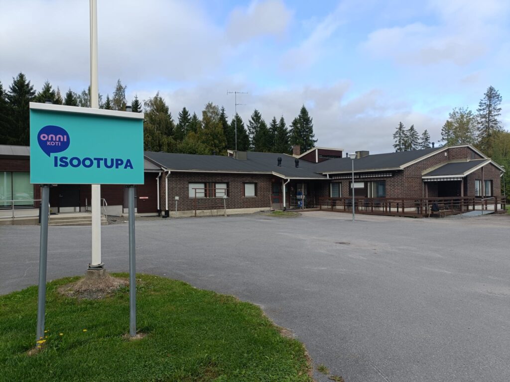 Onnikoti Isoo-tupa-kyltti onnikodin pihalla, iso ruskea rakennus