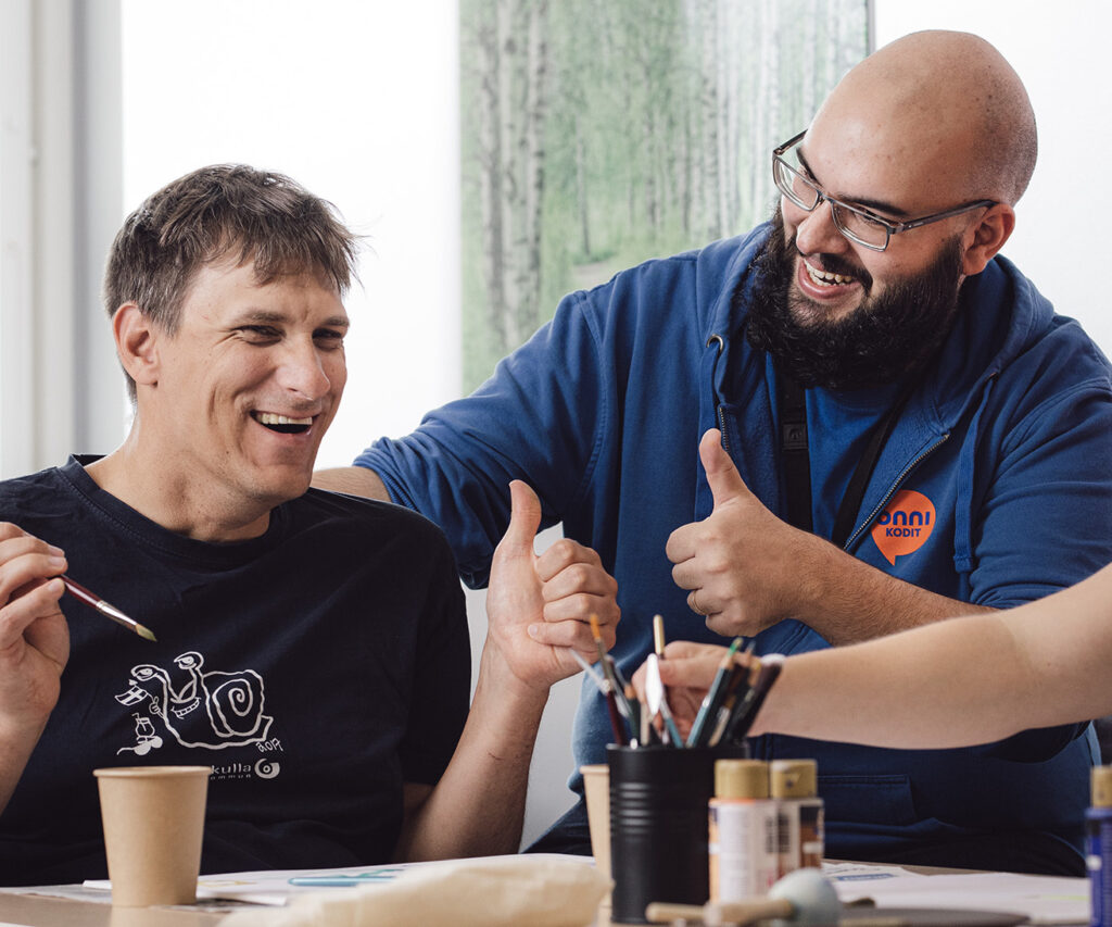 Ohjaaja ja asukas maalaavat yhdessä. Siveltimiä ja papereita pöydällä.