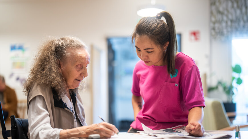 Lähihoitaja ja asukas tekevät ristisanatehtäviä yhdessä pöydän ääressä
