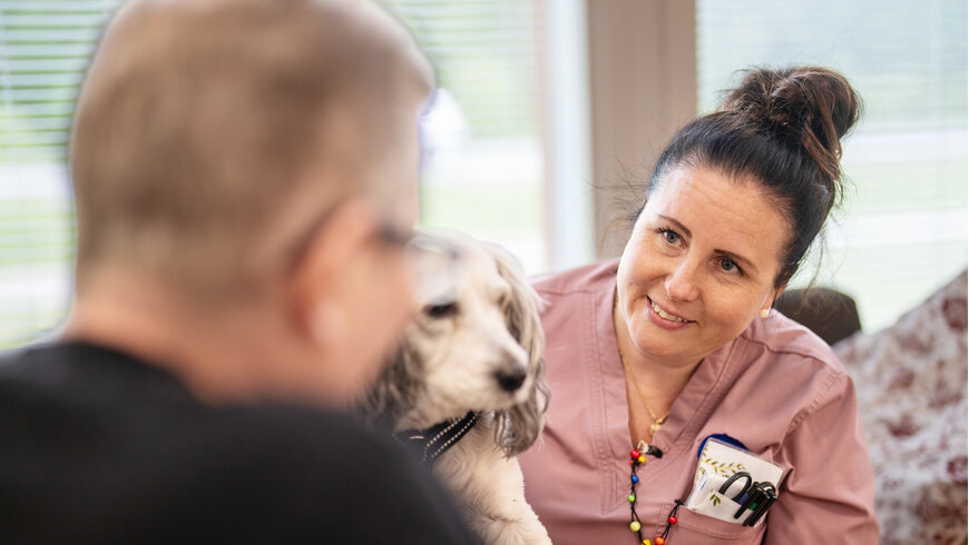 Onnikodin ohjaaja katselee vastapäätä istuvan henkilön sylissä olevaa koiraa