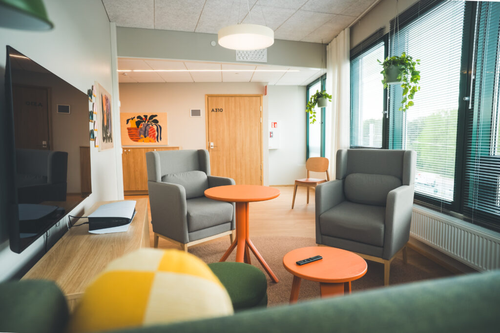 Fredrikin oleskelutila, kaksi harmaata nojatuolia, oranssit pikkupöydät.