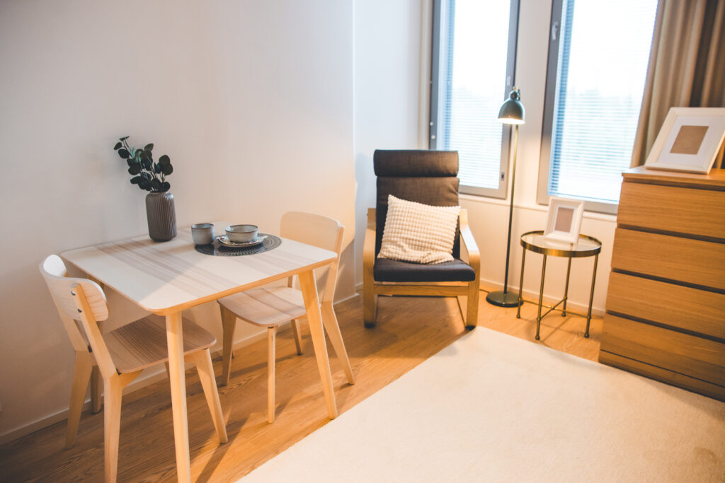 Asukashuone, vaalea puinen kahden hengen ruokailuryhmä, nojatuoli, lipasto.