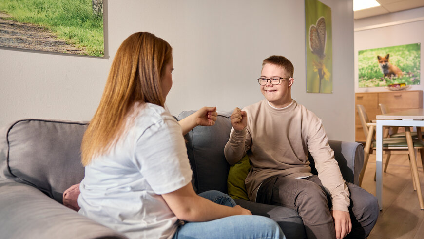 Nainen ja mies istuvat sohvalla Onnikodissa ja lyövät nyrkkejä yhteen hymyillen