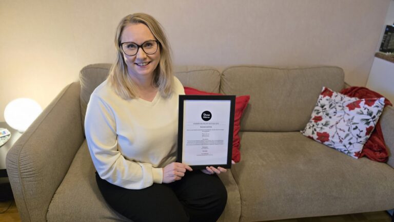 Minna Juuri-Oja istuu sohvalla kehystetyn kunniakirjan kanssa