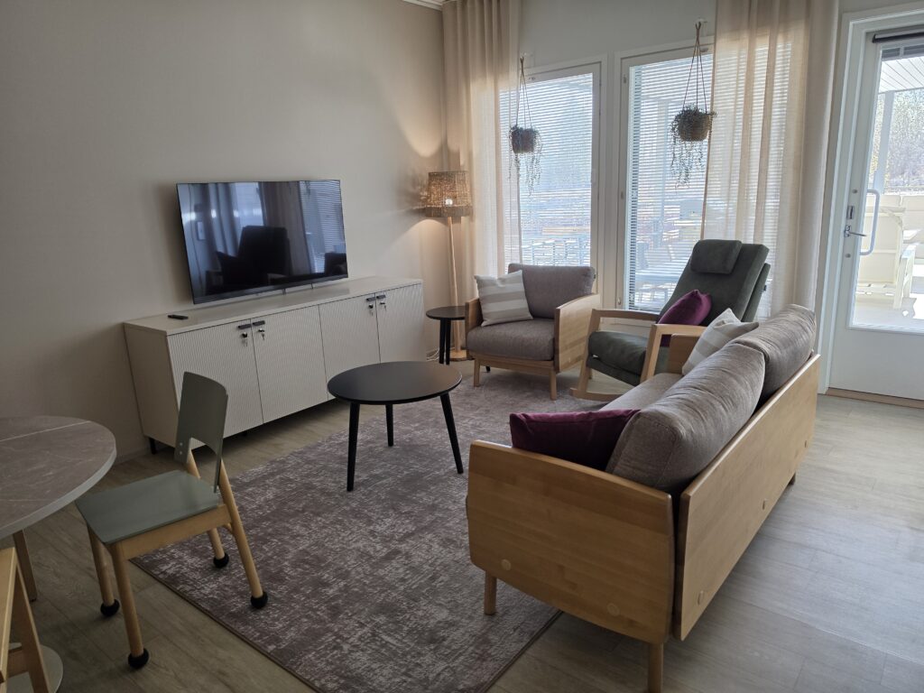 Valoisa huone, jossa on sohva, nojatuoleja ja televisio.