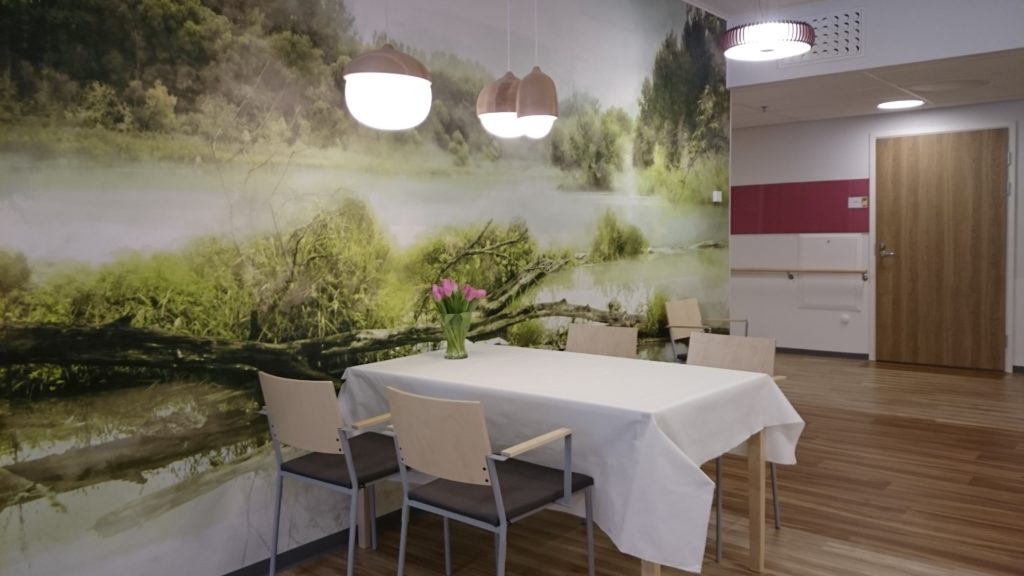 Onnikoti Alvarin tila, jossa on ruokailuryhmä ja seinällä suuri luontokuvamaisema.